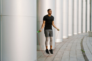 Black sportsman working out with jumping rope outdoors