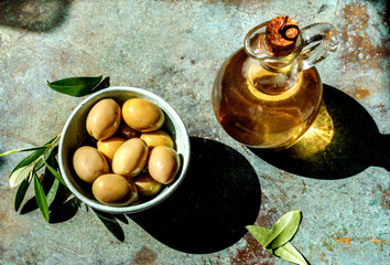 Bottle of of olive oil with fresh olives and olive branch on vinttage green table. Top view of...