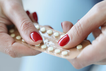 Woman with red manicure holding blister with contraceptive hormonal pills in her hands closeup - obrazy, fototapety, plakaty