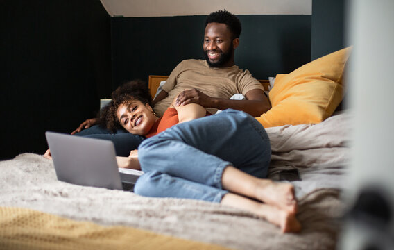 Young Adult Couple Looking At A Laptop Together In Bed