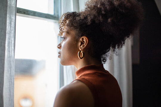 African american female looking out of window in home