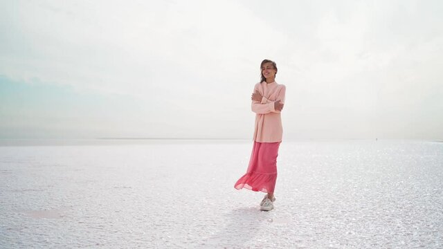 wonderful dreamy woman in big sweater and pink dress posing at windy salty coastline on pink salt lake.