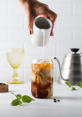 Cream is poured into cold black coffee with ice cubes. Coldbrew. Summer drinks.