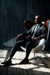 Stylish attractive african american businessman in a suit sits on a chair in the office and looks...