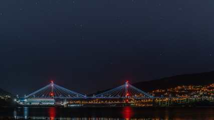 Fototapeta na wymiar illuminated bridge over the sea bay and sky night and stars with city in background