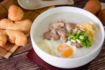 Hot Chinese congee (rice porridge) with minced pork ball and boiled egg as breakfast on wooden table