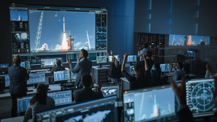 Group of People in Mission Control Center Witness Successful Space Rocket Launch. Flight Control Employees Sit in Front Computer Displays and Monitor the Crewed Mission. Team Stand Up and Clap Hands. © Gorodenkoff