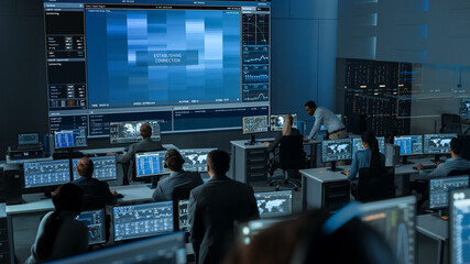 Group of People in Mission Control Center Trying to Establish Video Connection on a Big Screen with an Astronaut on Board of a Space Station. Flight Control Scientists Sit in Front Computer Displays. - Powered by Adobe