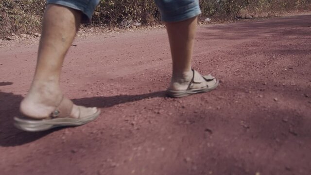 Close up shot of a man's feet as he strolls down a rural dirt road.