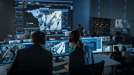 Female Officer Works on a Computer with Surveillance CCTV Video Footage in a Police Monitoring...