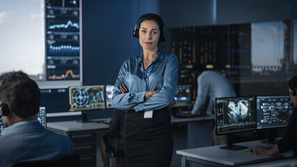 Portrait of a Beautiful Female Flight Controller Posing for Camera in a Mission Control Center. Successful Woman Wearing a Headset and Crossing Her Arms. Computer Screens in the Background.