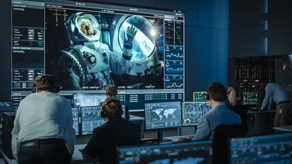 Group of People in Mission Control Center Establish Successful Video Connection on a Big Screen with an Astronaut on Board of a Space Station. Flight Control Scientists Sit in Front of Computers.