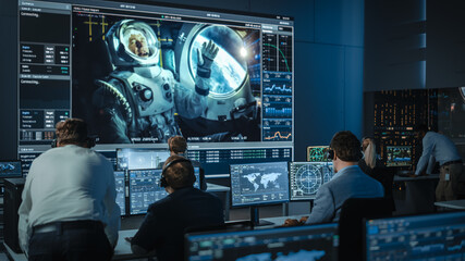 Group of People in Mission Control Center Establish Successful Video Connection on a Big Screen with an Astronaut on Board of a Space Station. Flight Control Scientists Sit in Front of Computers. - Powered by Adobe