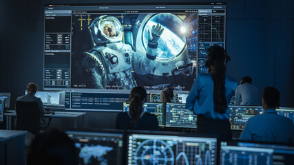 Group of People in Mission Control Center Establish Successful Video Connection on a Big Screen with an Astronaut on Board of a Space Station. Flight Control Scientists Sit in Front of Computers.