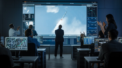 Group of People in Mission Control Center Witness Successful Space Rocket Launch. Flight Director is Pacing Nervously in Front of the Screen and Punches the Air in Celebration. Team Claps Hands.