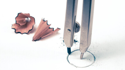 Macro detail closeup of a school geometry drawing compass drafting a round circle on white student paper with study pencil shavings in the background, with copyspace