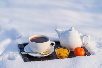 Obraz na płótnie Canvas White cup of hot tea and teapot on a bed of snow and white background, close up