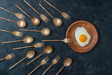 Ceramic plate with fried egg and brass forks and spoons look like sperm competition. Spermatozoons floating to ovule - obrazy, fototapety, plakaty