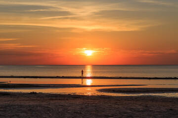 Fototapeta na wymiar orange sunset in the evening on the baltic sea and silhouette of a man