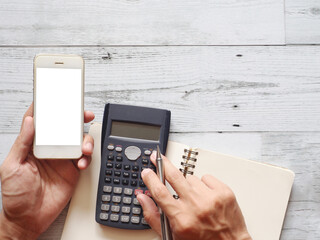 Hand holding mobile phone white screen and using calculator with cactus and silver pen on white wood table nature shadow and sunlight top view and space business concept