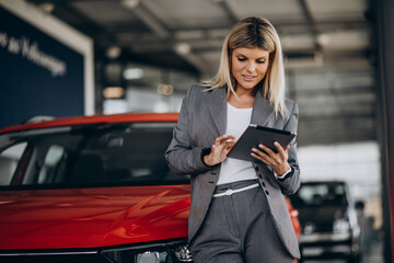 Pretty woman with tablet in car showroom