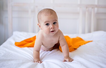 baby girl in a diaper and with an orange towel crawls on the bed. Child development
