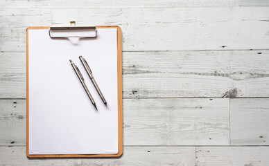 Two silver pen on blank white document sheet on wood clipboard on white wood table top view space