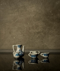 Small kids toy porcelain set on reflective surface with concrete wall background. Old, vintage and antique sets funny idea. Minimal relaxing concept.