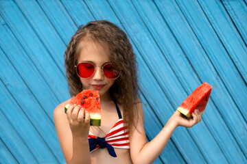 A beautiful girl savors a piece of ripe juicy sweet watermelon with pleasure. Curly stylish girl in...