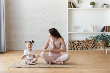 mother in pink outfitt and small kid girl practicing lotus yoga with mudra hands pose and namaste gesture