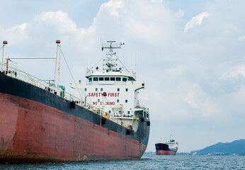 Fototapeta premium Big logistic ship unloading in the ocean with view mountain on island background and cloudy on sky,Shipping boat economy transportation concept on the sea