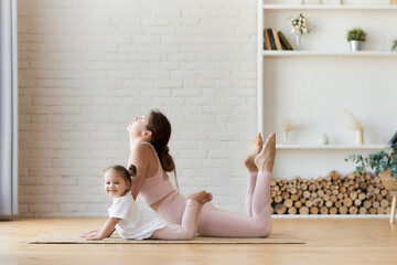 Little girl looks at the camera and smiles, repeating her body flexibility exercises after her mother