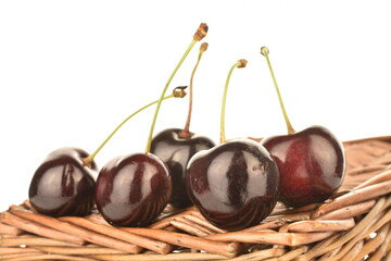 Several juicy berries of dark red cherries on a vine mat, close-up, isolated on white.