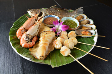 mixed bbq grill seafood scallop stick, octopus, prawn, fish, muscle shell in spicy chili sauce on banana leaf asian halal menu