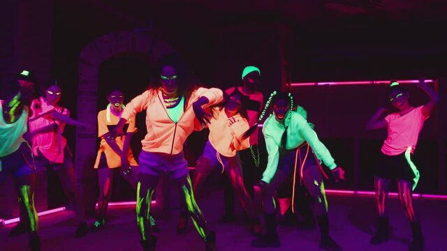 4K Group of female and male stylish dancers dancing inside dark place with neon lights .  Beautiful young people with fluorescent colorful make-up and clothes dancing in UV light. HD video slow motion