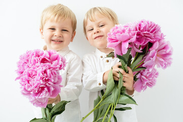 two cute child blonde twins boys with big bouquet of pink peonies smiling on white background