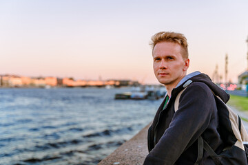 A young man stands on the embankment in St. Petersburg at sunset with a view of St. Isaac's Cathedral