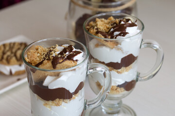 Dessert of biscuits, cream and chocolate. Next to it is a biscuit and cream sandwich. Decorated with chocolate. Lies on a plate.