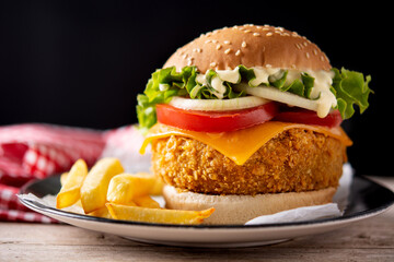 Crispy chicken burger with cheese and french fries on wooden table	