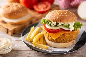 Crispy chicken burger with cheese and french fries on wooden table	