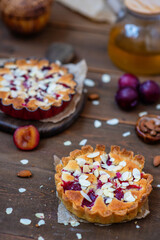 Sandy plum tarts with frangipan and almond petals on a wooden background with plum decor.