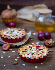 Sandy plum tarts with frangipan and almond petals on a wooden background with plum decor.