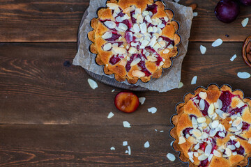 Plum cake on a shortbread basis with frangipan and almond petals on a wooden background. Place for text