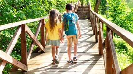 Children are heading to the family campsite in the forest along the equipped wooden deck. Walk along the tourist route with a backpack on your back. Camping road. Family travel vacation concept.