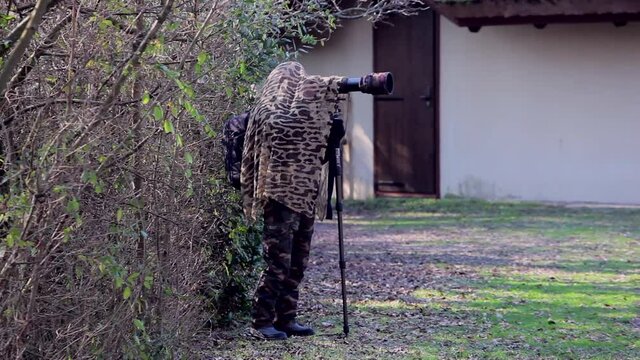 Bird photographer wearing camouflage cape take photos with a camera and telephoto, Laguna di Marano