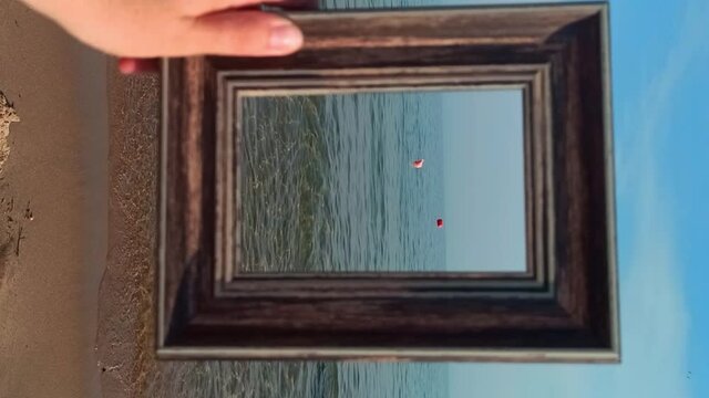 Femele hand holding Empty Photo frame on sandy sea beach. Travel Summer memories concept. Vertical video format