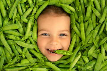 The face of a cute funny child, surrounded by green pods of fresh ripe peas. Healthy proper...