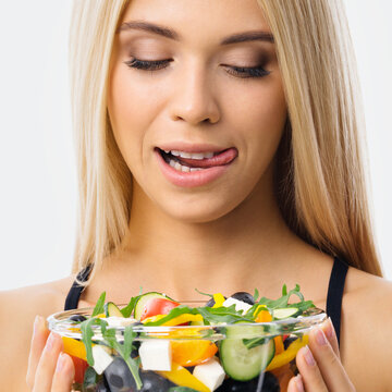 Image of blond woman with tongue lick mouth, looking at glass plate of greece salad. Blonde girl at studio. Keto diet, ketogenic weigh loss, vegetarian concept. Square composition.