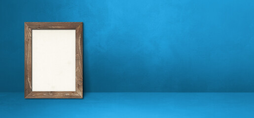 Wooden picture frame leaning on a blue wall. Horizontal banner