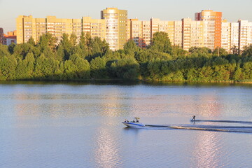 A boat with a water skier on the river An against the background of residential buildings, Dubna,...